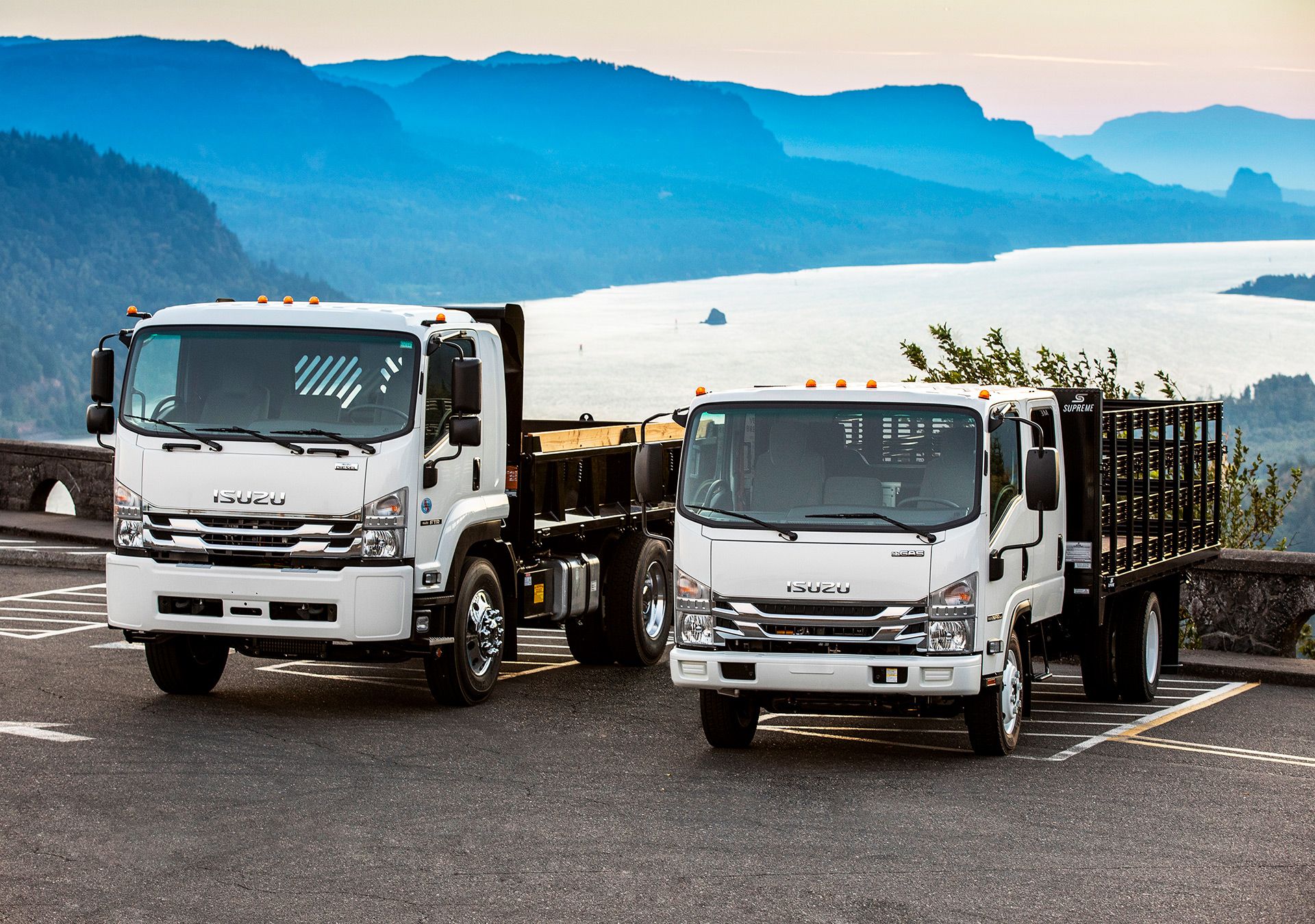 Two Isuzu Commercial Trucks parked with mountains and lake in background